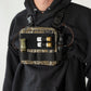A man wearing a black hoodie and a chest rig bag with a camouflage pattern, holding shotgun shells and a bottle.